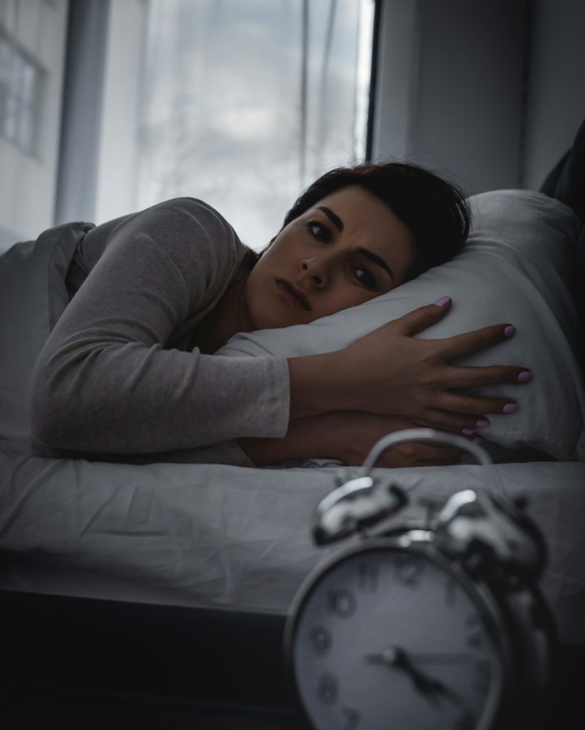 selective focus of awake woman looking at alarm clock on bedside table